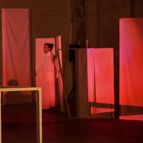 Performer Fanis Sakellariou is trapped in a set element which are projected on with images in red